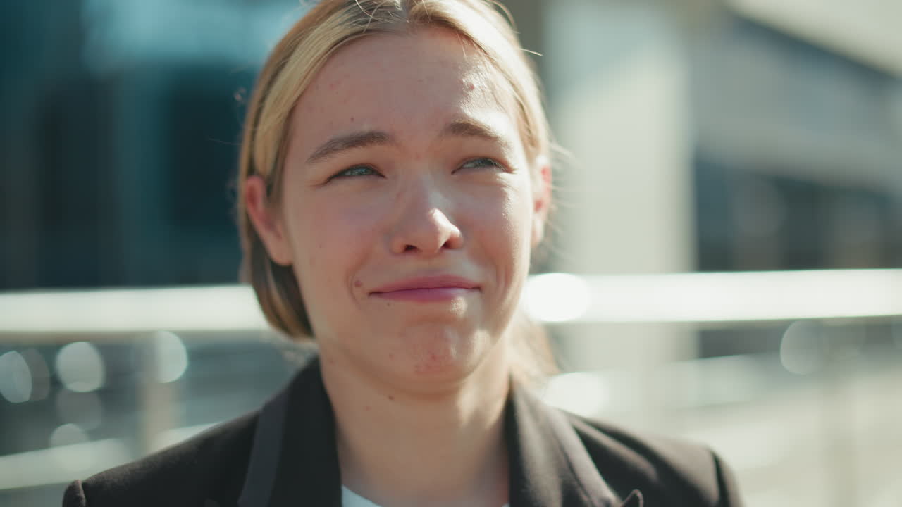 Upset lady in formal outfit crying silently outdoors, overwhelmed by emotion, walking near railing with modern glass building reflecting sunlight in background