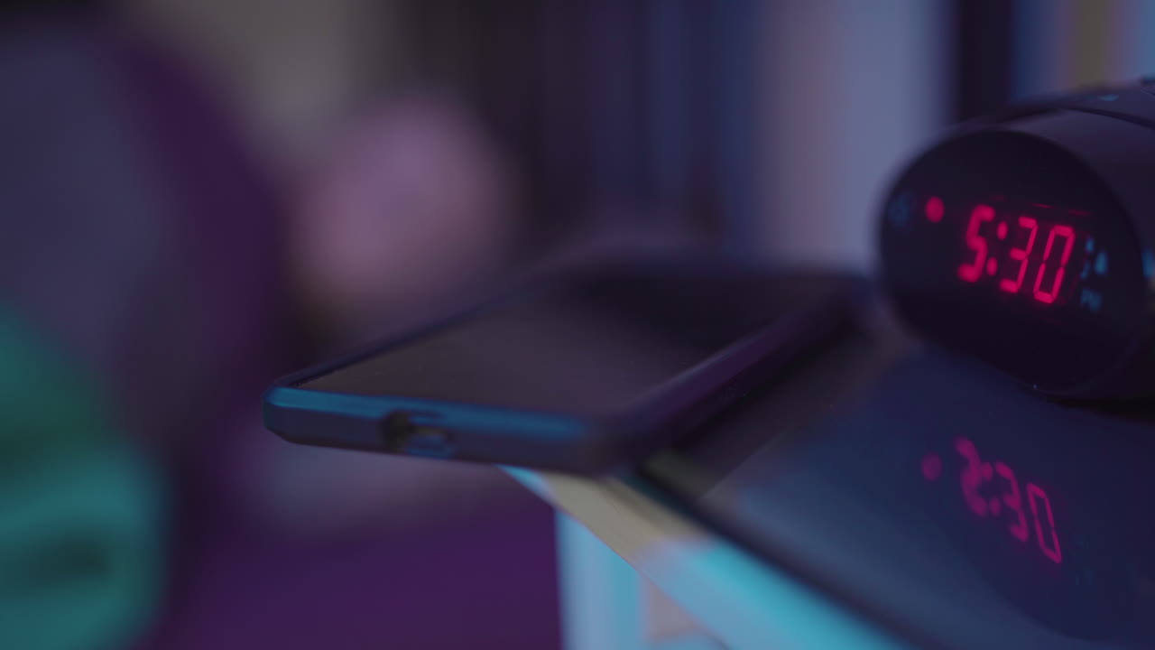 el despertador suena a las 5:30 a. m. y la persona que duerme en segundo plano busca su teléfono y comienza el día deslizándolo