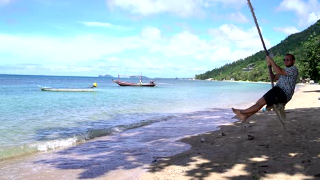 the man in sunglasses swinging on a rope on the beach on the seashore