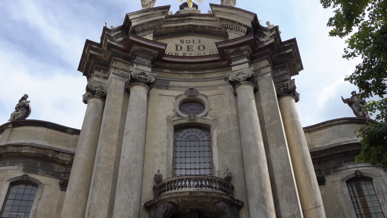 Ukraine, Lviv, Church of the Holy Eucharist's front facade on a sunny day with blue skies and white clouds, people chatting in front of the beautiful building. Camera tilts up from street level to sky