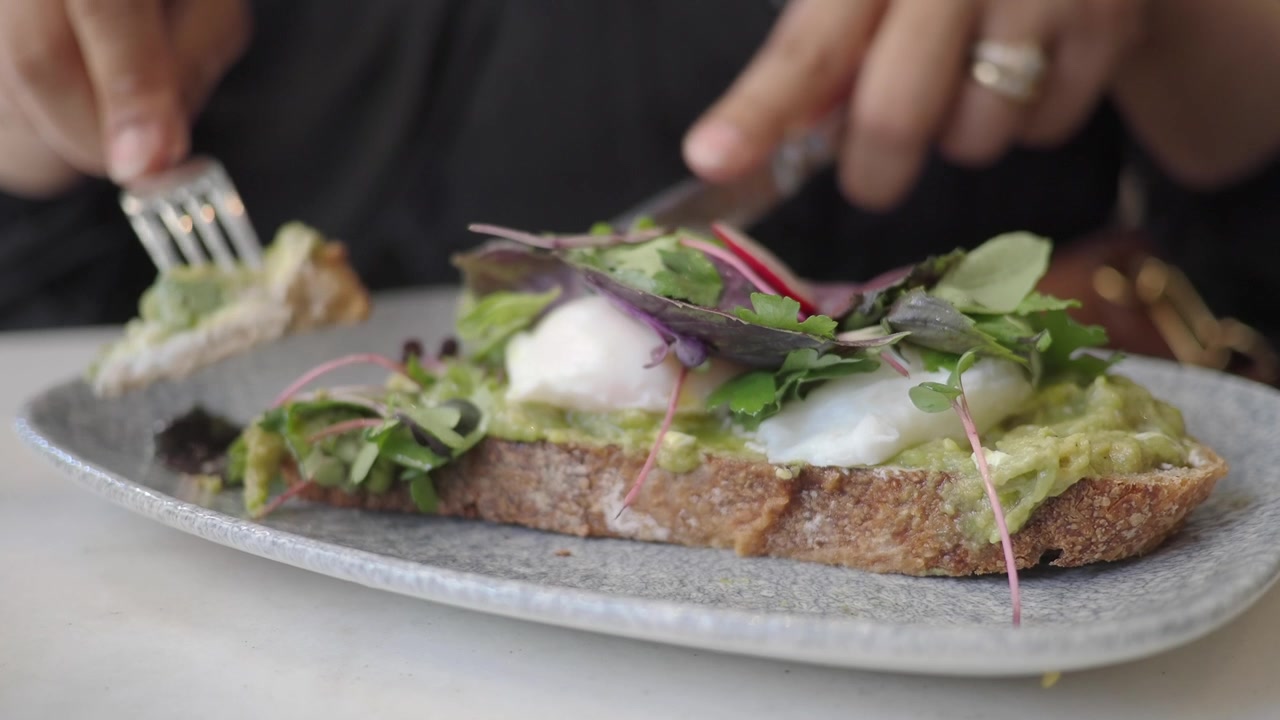Person Eating Avocado Toast with Poached Egg in Restaurant