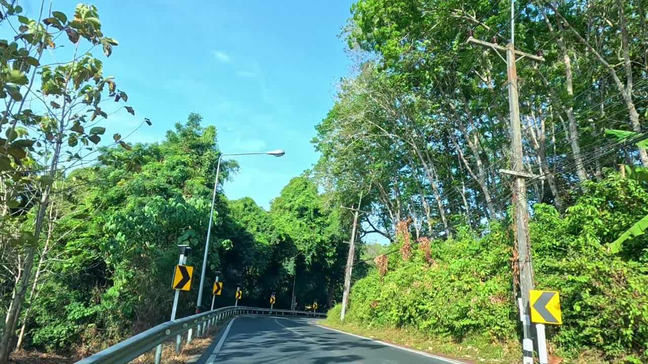 A 20-second drive along a verdant, winding road in Phuket, Thailand, under clear blue skies and bright daylight
