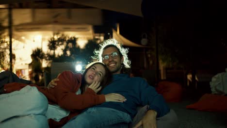 Close-up-shot:-a-couple-in-love-are-lying-on-beanbag-chairs-and-watching-a-movie.-A-party-outside-the-city.-Rest-in-the-country-house