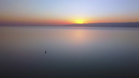 Drohnenaufnahmen-Vom-Fliegen-über-Einen-Großen-See-Und-Schwenken-Um-Ein-Segelboot-Bei-Sonnenuntergang,-Mit-Einem-Großen-Berg-Im-Hintergrund