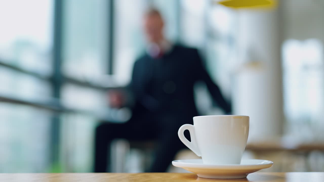 White cup of coffee on the table in the office. Coffee cup on the blur background of a businessman working with papers.