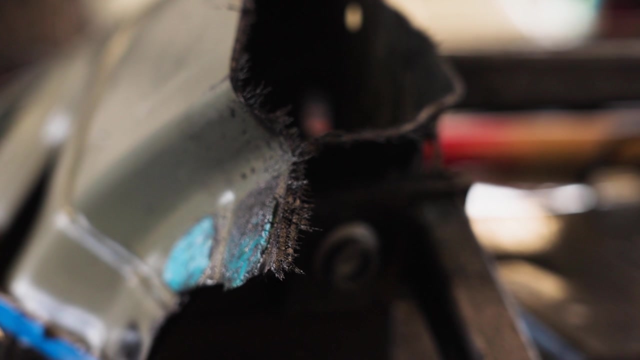 Sharp metal shards and cut vehicle panel detail during automotive repair or an industrial cutting process in a workshop environment with shallow depth of field, UHD.