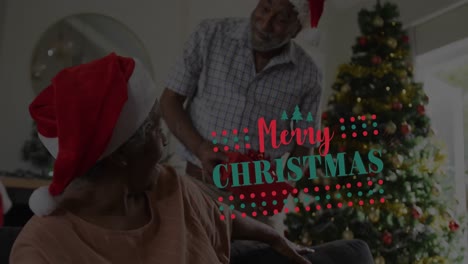 Animación-De-Texto-De-Feliz-Navidad-Sobre-Una-Pareja-Afroamericana-De-Alto-Nivel-Con-Gorros-De-Papá-Noel