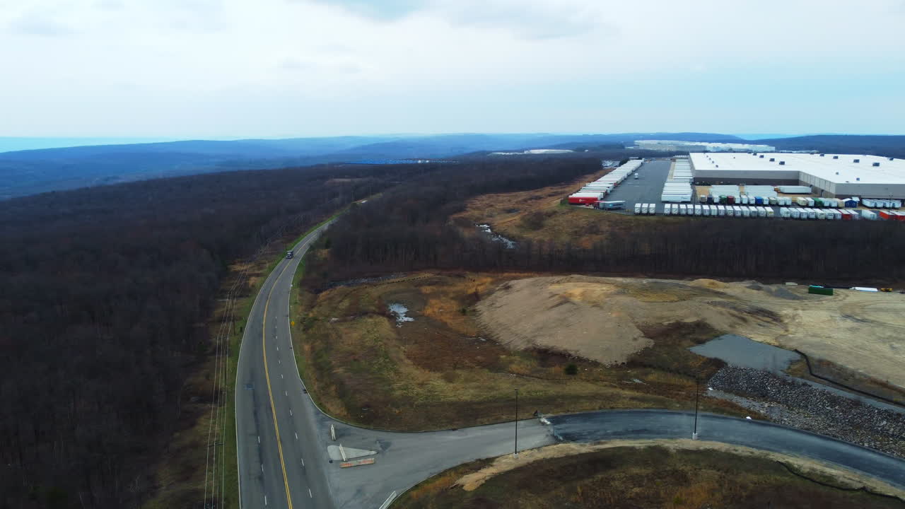 A cinematic drone push-in on a Schuylkill County shipping center, framed by distant mountains, rows of containers, warehouses, and nearby cars and trucks moving along active surrounding roads.