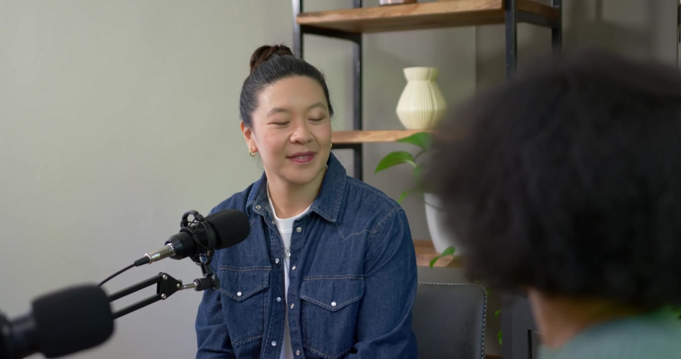 Donna asiatica che ascolta e poi risponde dopo che un intervistatore afroamericano parla al microfono in studio.