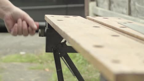 workman hand manually turning the handle of a wooden workbench