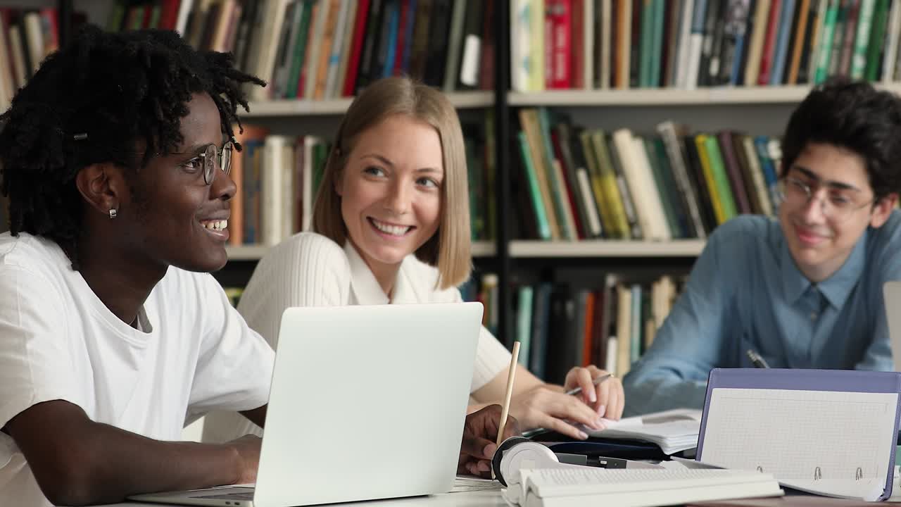 Diverse students sit at desk in library preparing for exams