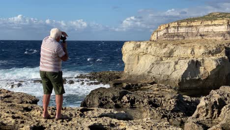 Hombre-Mayor-No-Identificable-Mira-A-Través-De-La-Cámara-En-La-Costa-De-Gozo,-Malta--Agujero-Azul,-Dwejra