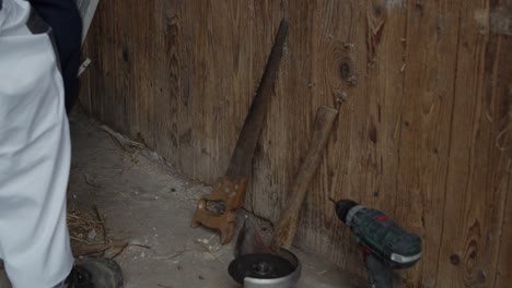 Worker-Places-Old-Tools-Next-To-Wooden-Wall,-Farm