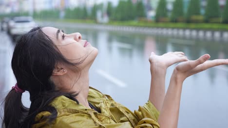 young beautiful asian female put on the hoody of yellow raincoat after using hands catching falling rains, rainy season weather, stormy sorrow, unlucky days, bad luck, urban street on the back ground