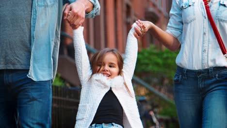 Couple-swing-their-daughter-as-they-walk-in-street,-mid-section