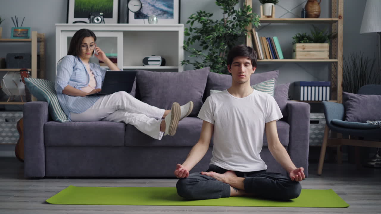 Couple relaxing at home. Man meditating, woman on phone call.