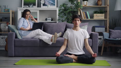 couple relaxing at home. man meditating, woman on phone call.