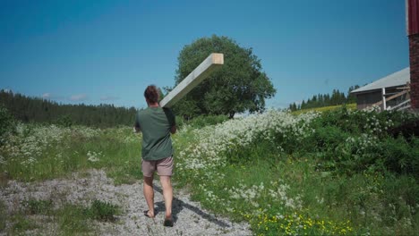 a man is carrying a block of wood on a sunny breeze day in rural nature landscape