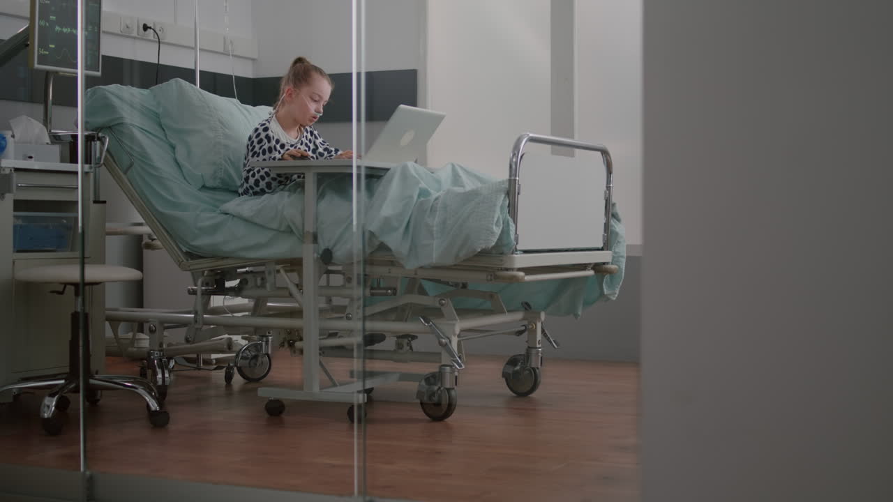 Sick child relaxing in bed playing cartoon video games on laptop computer during medical examination