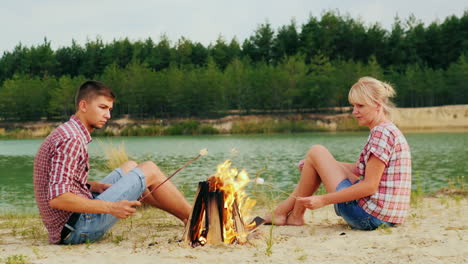 Freunde-Eines-Mannes-Und-Einer-Frau-Sitzen-Am-Lagerfeuer-Gebratene-Marshmallows-Auf-Stöcken-Gegen-D