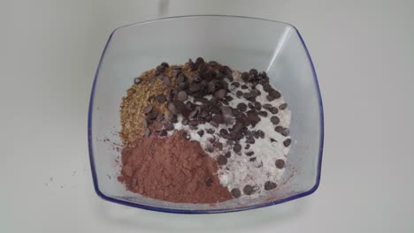 dropping chocolate chips into mixture of dry cookie ingredients