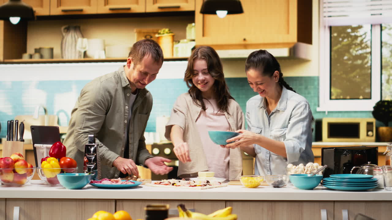 Parents and tween girl laughing while sprinkling mozzarella on pizza