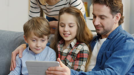 Cerca-De-La-Familia-Feliz-Con-Niños-Sentados-En-El-Sofá-Y-Abrazándose-Mientras-Ven-Algo-En-La-Tableta