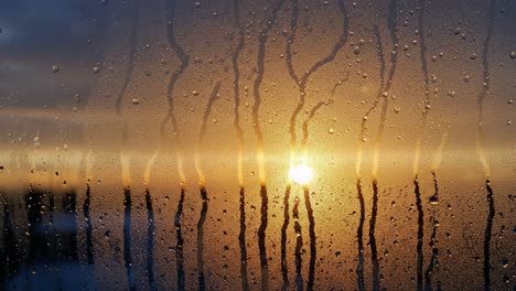 a beautiful sunset through a foggy window with raindrops, creating a moody atmosphere as nature's colors blend and reflect off the glass surface