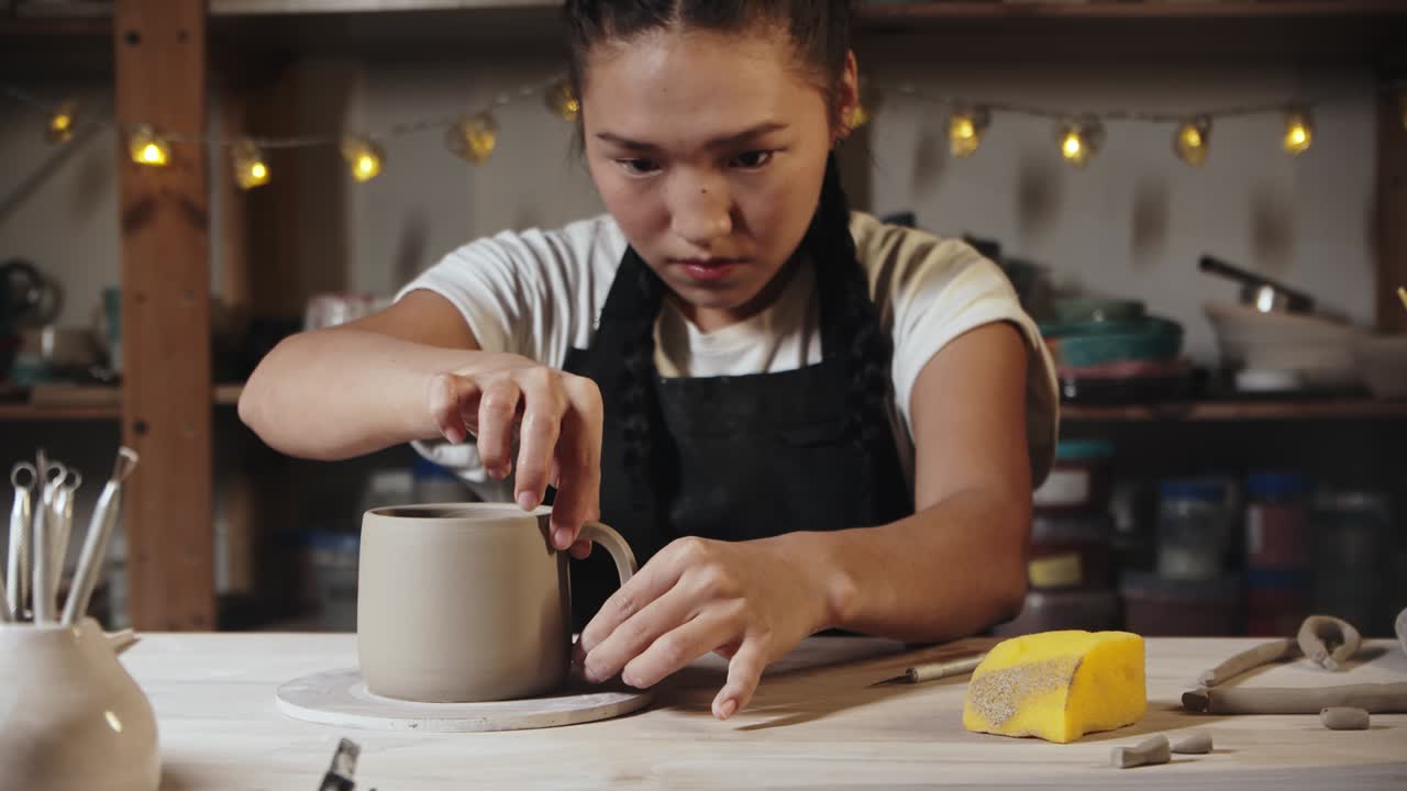 joven alfarera tratando de un mango de arcilla a una taza en el estudio de arte