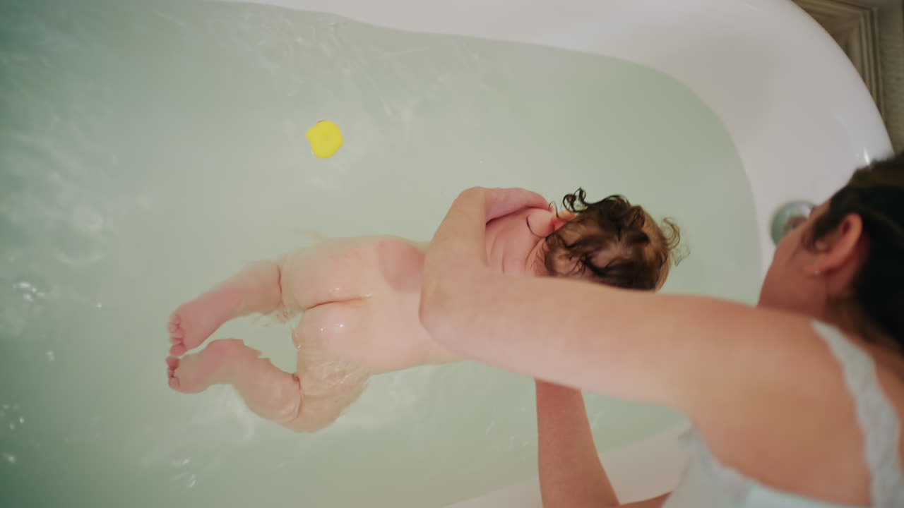 Top view of mother bathing baby in bathtub while playing with bath toys