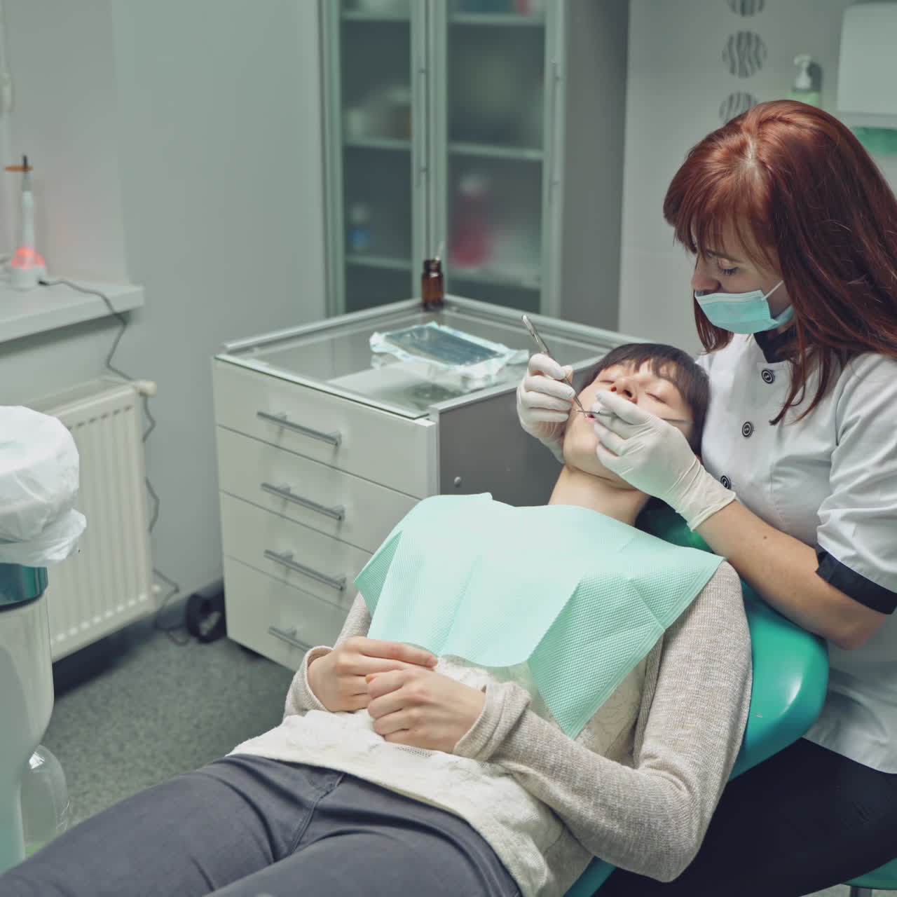 Woman patient on the inspection of the teeth in dentistry. Female dentist treats a girl's teeth in a light clean dental clinic