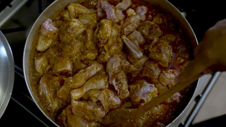 Vista dall'alto di pezzi di pollo mescolati in un ricco curry all'interno di una grande pentola.