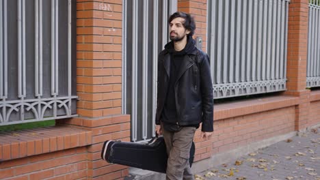 happy man holding a guitar case while walking