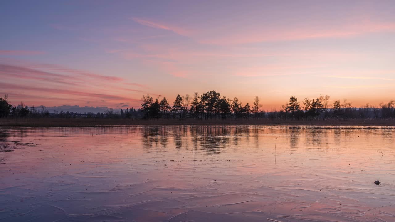 Pink red sunset on a landscape with frozen lake in the foreground. In the background you can see a mountain landscape and a nature reserve. It's winter and the mood is harmonious