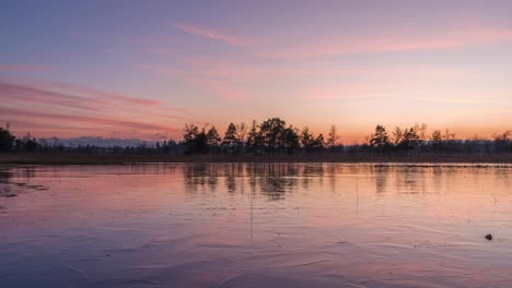 pink red sunset on a landscape with frozen lake in the foreground. in the background you can see a mountain landscape and a nature reserve. it's winter and the mood is harmonious