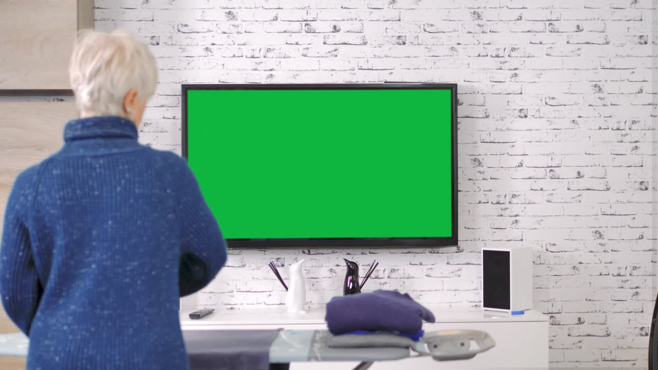 집안 일 을 하는 여자 가 녹색 스크린 으로 tv 를 보는 것