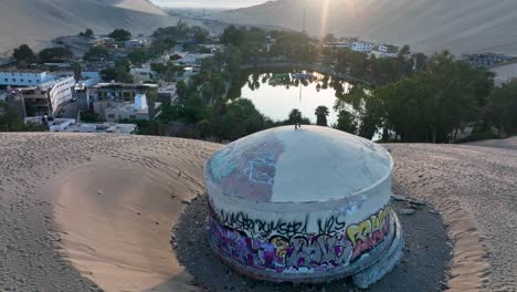 Oasis-Del-Desierto-Huacachina,-Perú-Con-Lago-Y-Palmeras,-Con-Grandes-Dunas-De-Arena-En-El-Fondo