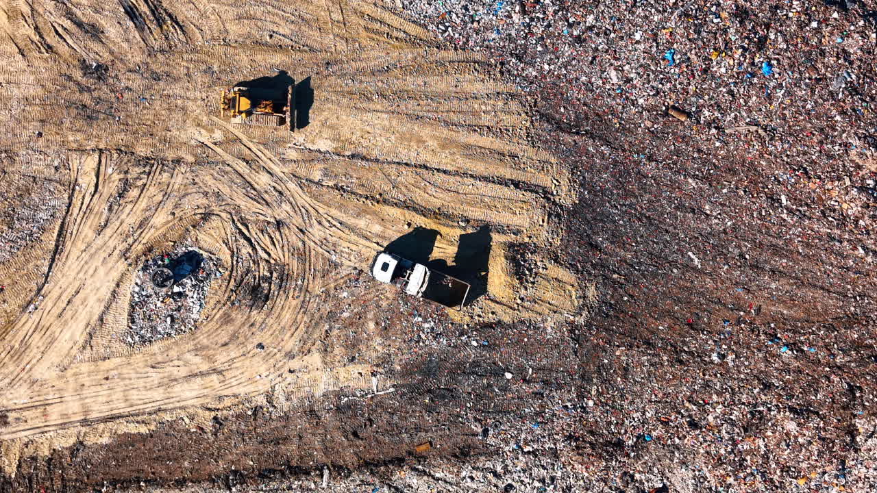 Attrezzature pesanti che operano su un sito di discarica su larga scala. Vista aerea dall'alto di un bulldozer e un camion che si muovono sul terreno di un impianto di gestione dei rifiuti.