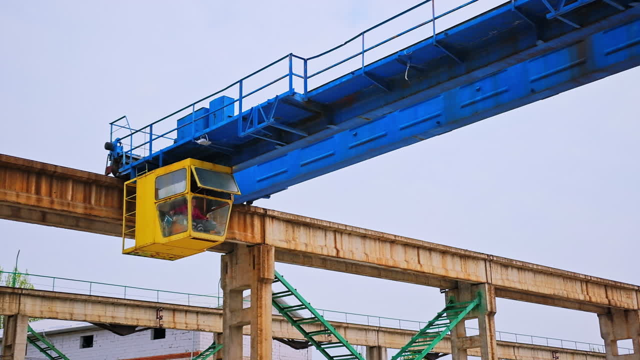 Yellow booth with a working person inside. Construction crane machinery at the backdrop of grey sky.