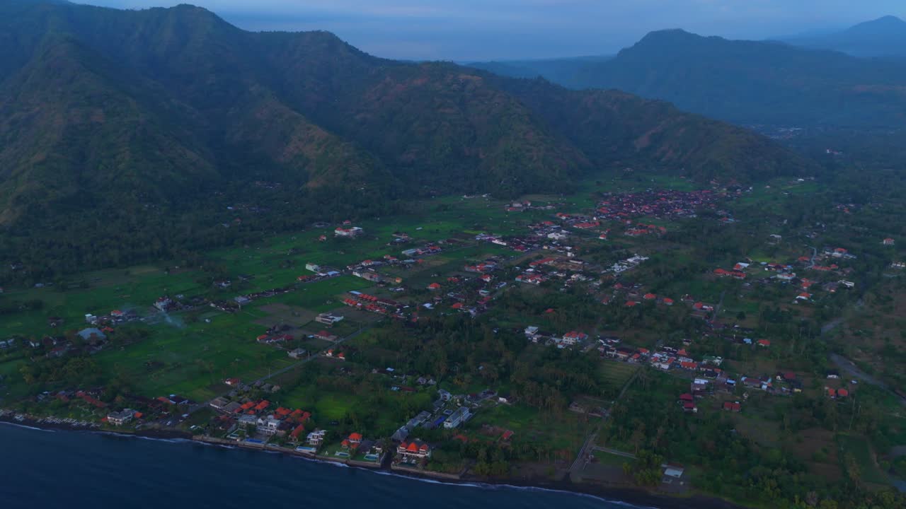 Aerial sunset over fishing harbor with village shoreline surrounding hills and anchored boats