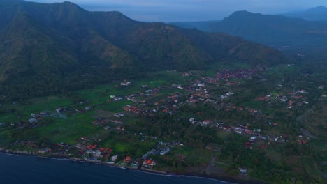 aerial sunset over fishing harbor with village shoreline surrounding hills and anchored boats