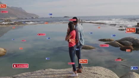 Standing-on-rocks-by-sea,-couple-with-social-media-buttons-animation