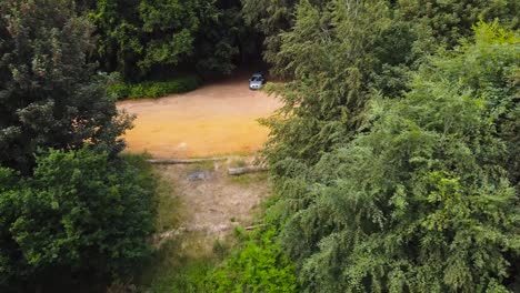 A-cinematic-aerial-push-back-shot-of-a-car-inside-a-forest-full-of-green-trees-near-Norfolk-England-morning