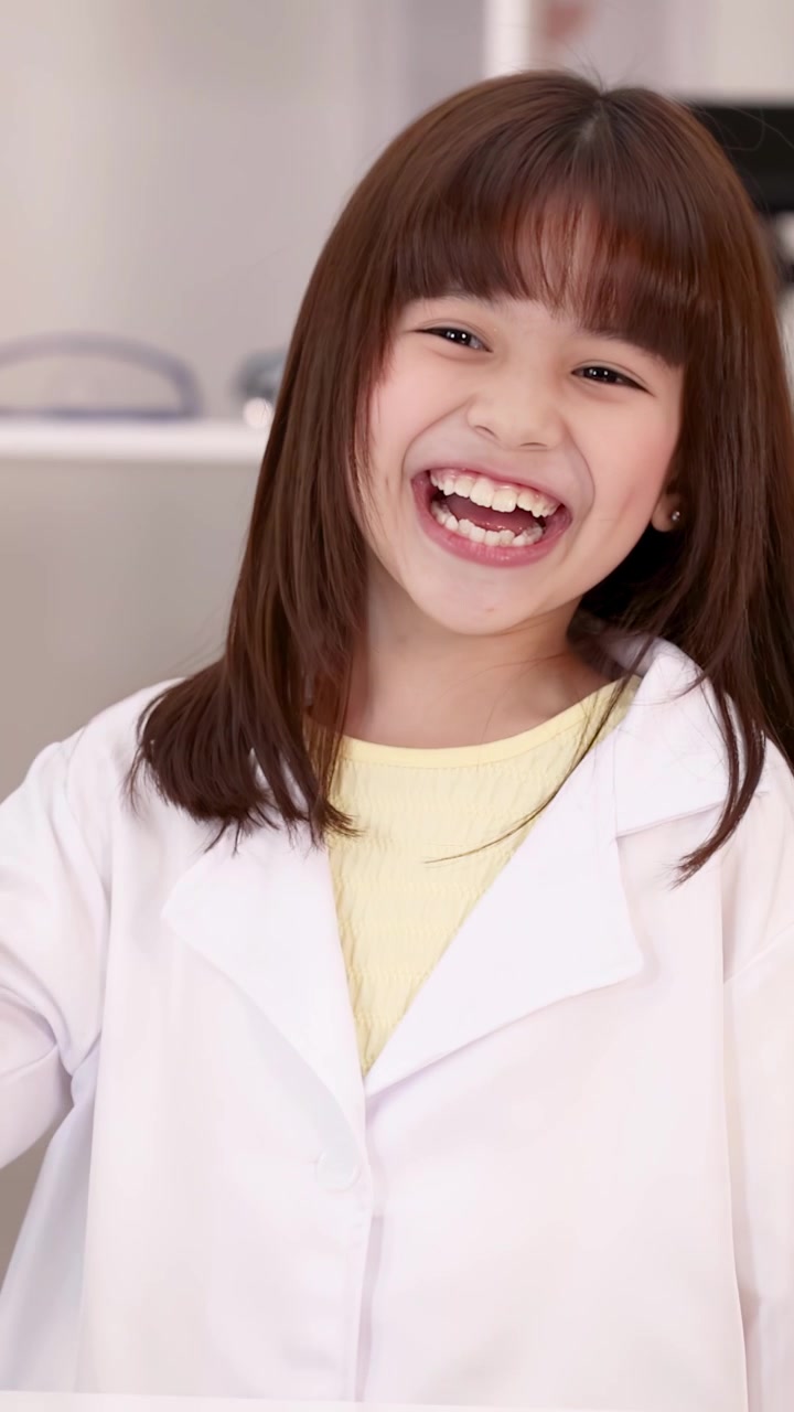 Một học sinh đang cười mặc áo khoác phòng thí nghiệm màu trắng cầm một chiếc kính lúp che miệng