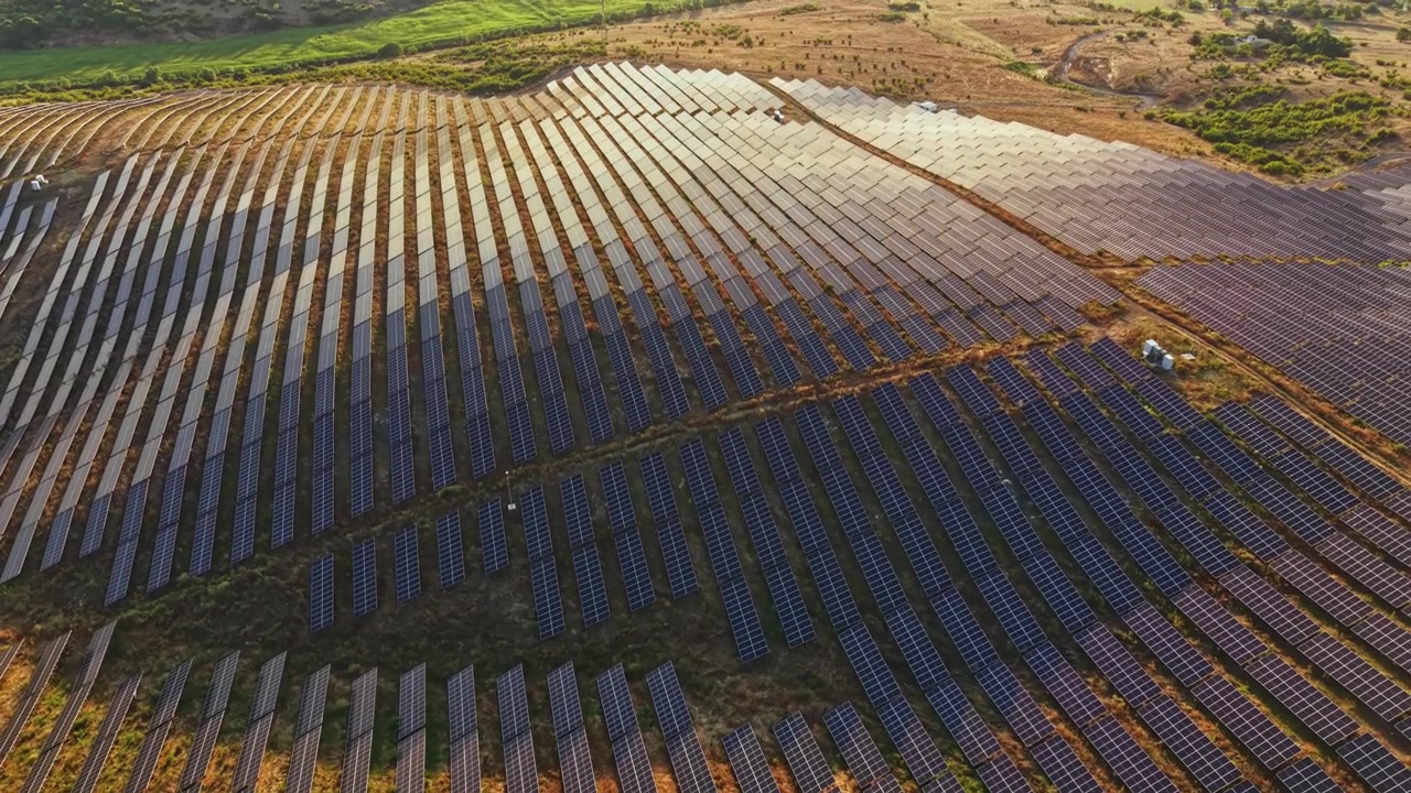 Solpaneler dækker et stort felt i et landområde i klart dagslys, der viser teknologi for vedvarende energi.