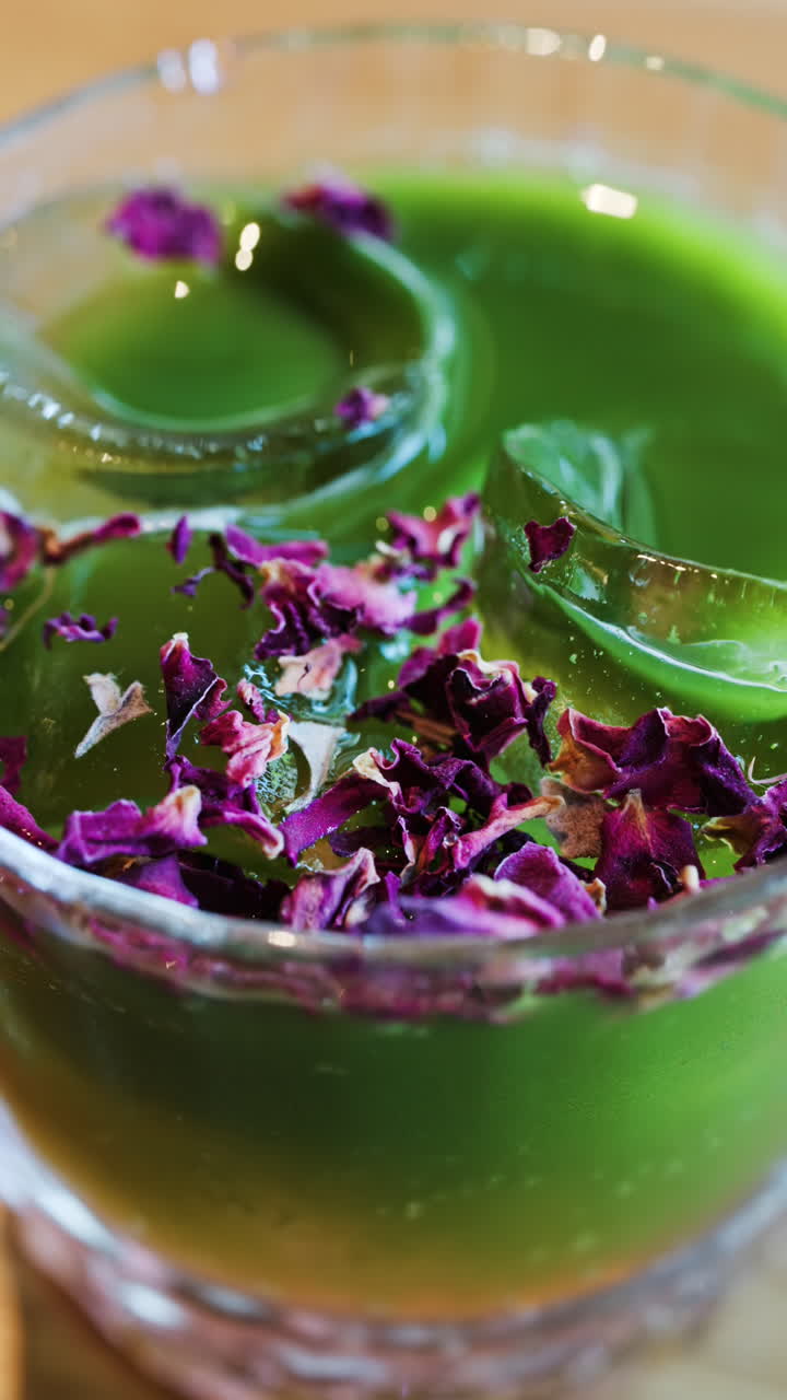 Close up of an iced matcha in a glass with purple dried flowers on top. Vertical