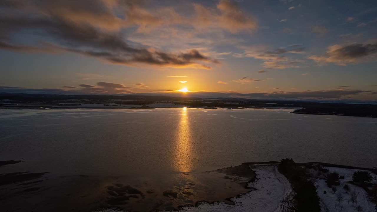 Aerial timelapse shot at sunset over a lake with a snow-covered shore
