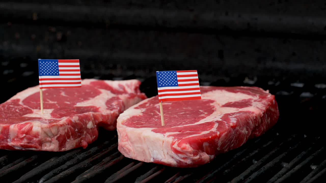 dos bistecs de rib-eye jugosos sentados en la parrilla y cocinados con dos diminutas banderas americanas metidas en ellos
