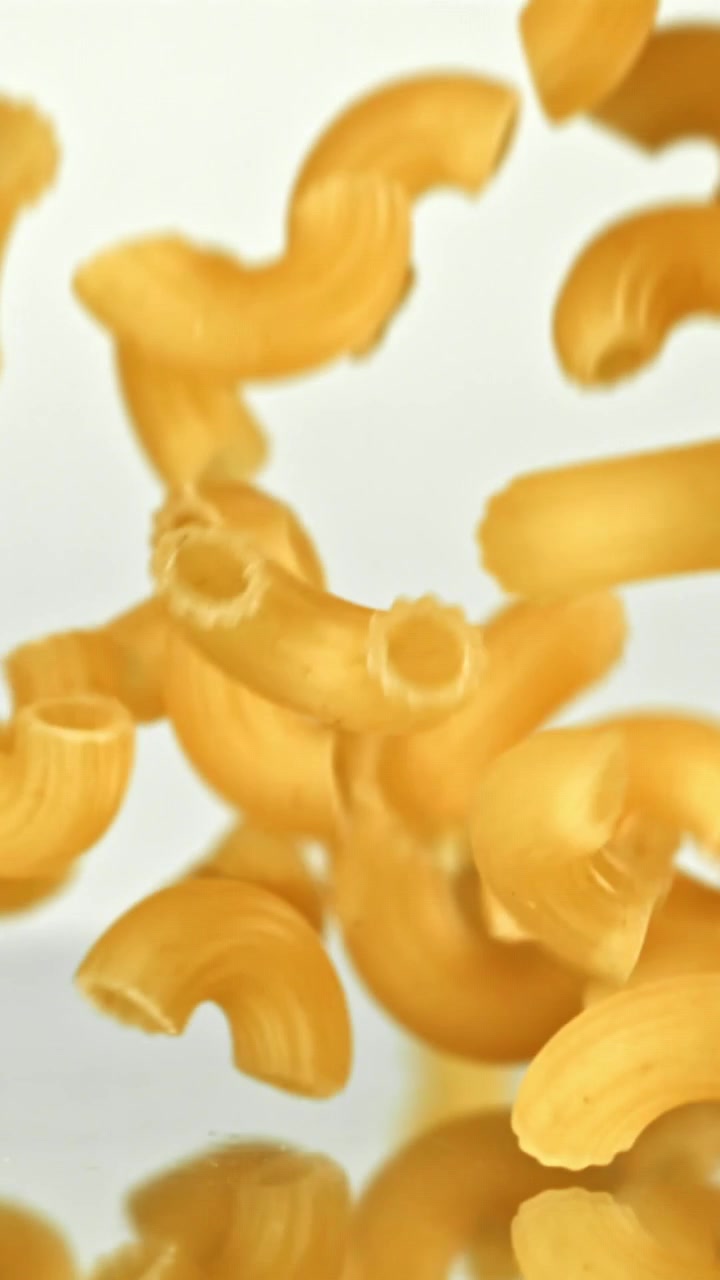 Maccheroni secchi in caduta al rallentatore su sfondo bianco