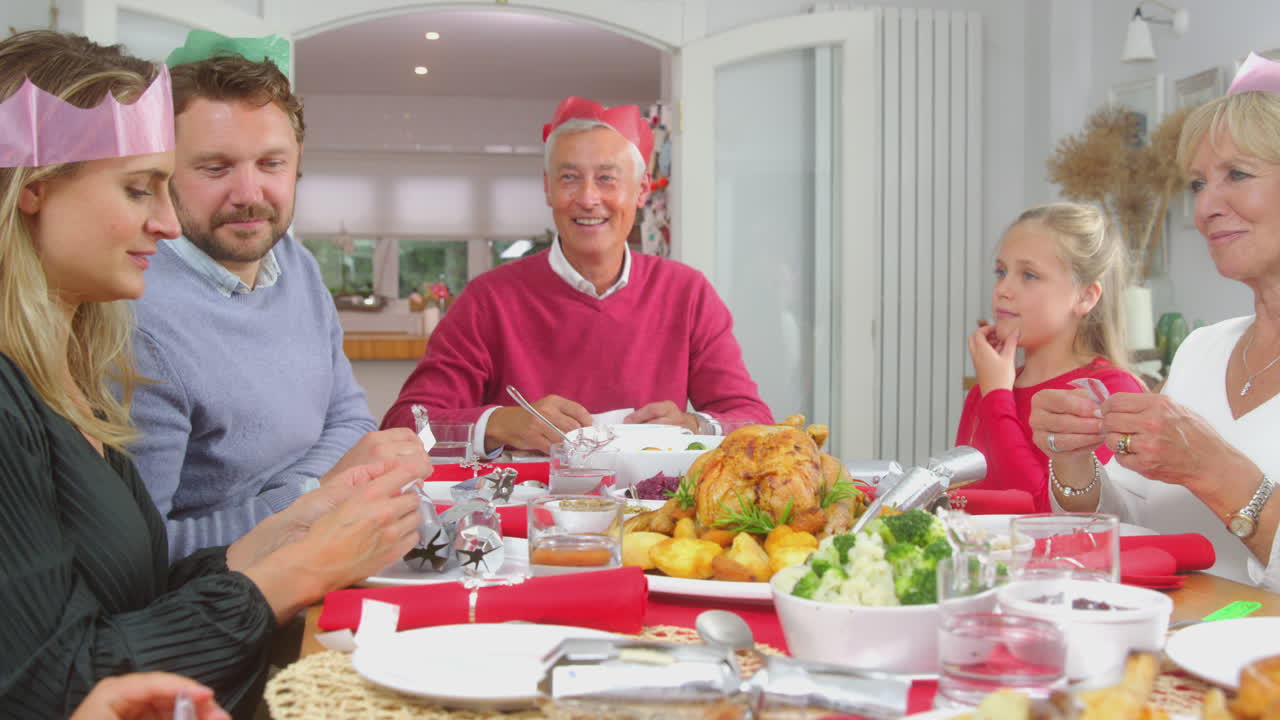 Flergenerationsfamilie med festhatte læser julejokes, mens de spiser middag sammen